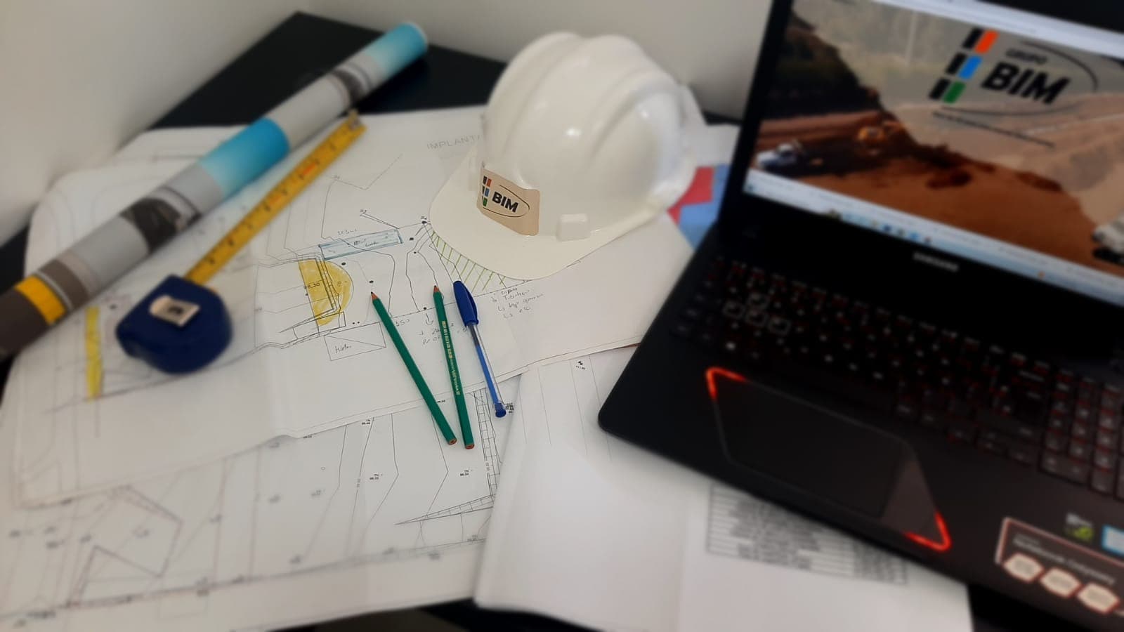 Projetos de engenharia, capacete e material técnico sobre uma mesa.
