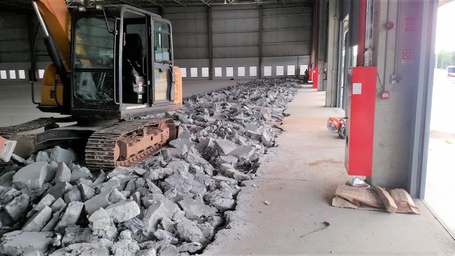 Escavadeira e concreto removido durante a demolição de um piso industrial.