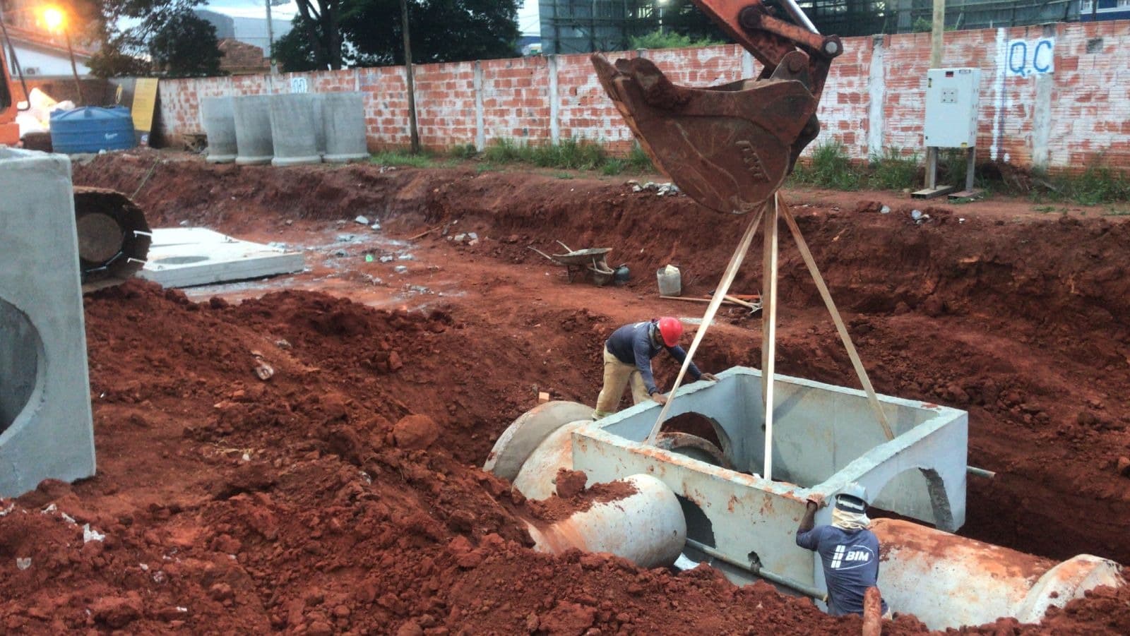 Instalação de uma estrutura de concreto para drenagem com auxílio de escavadeira.